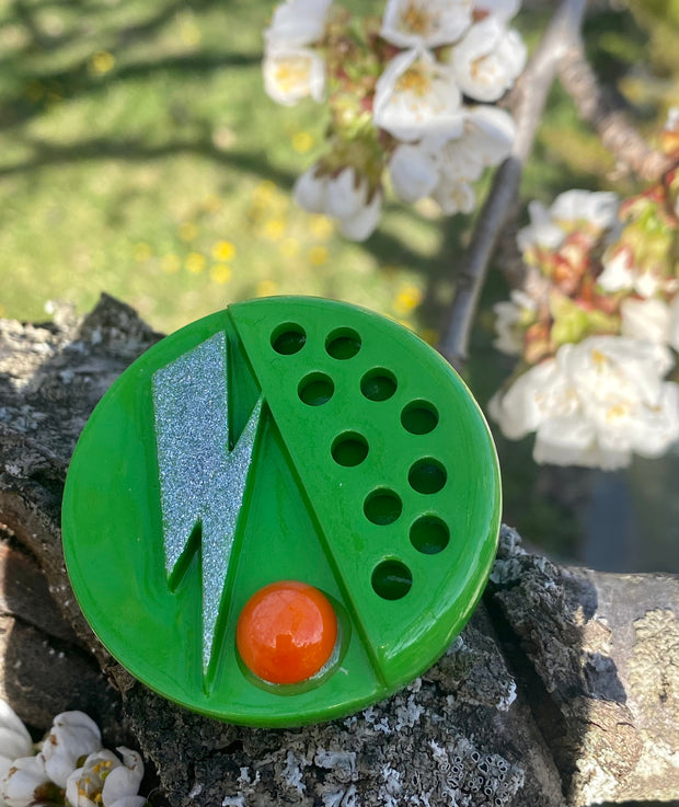 Broche verde con piedra naranja.